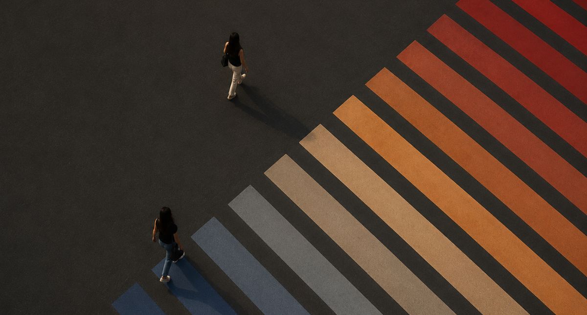A multi colored crosswalk with 2 people walking. 