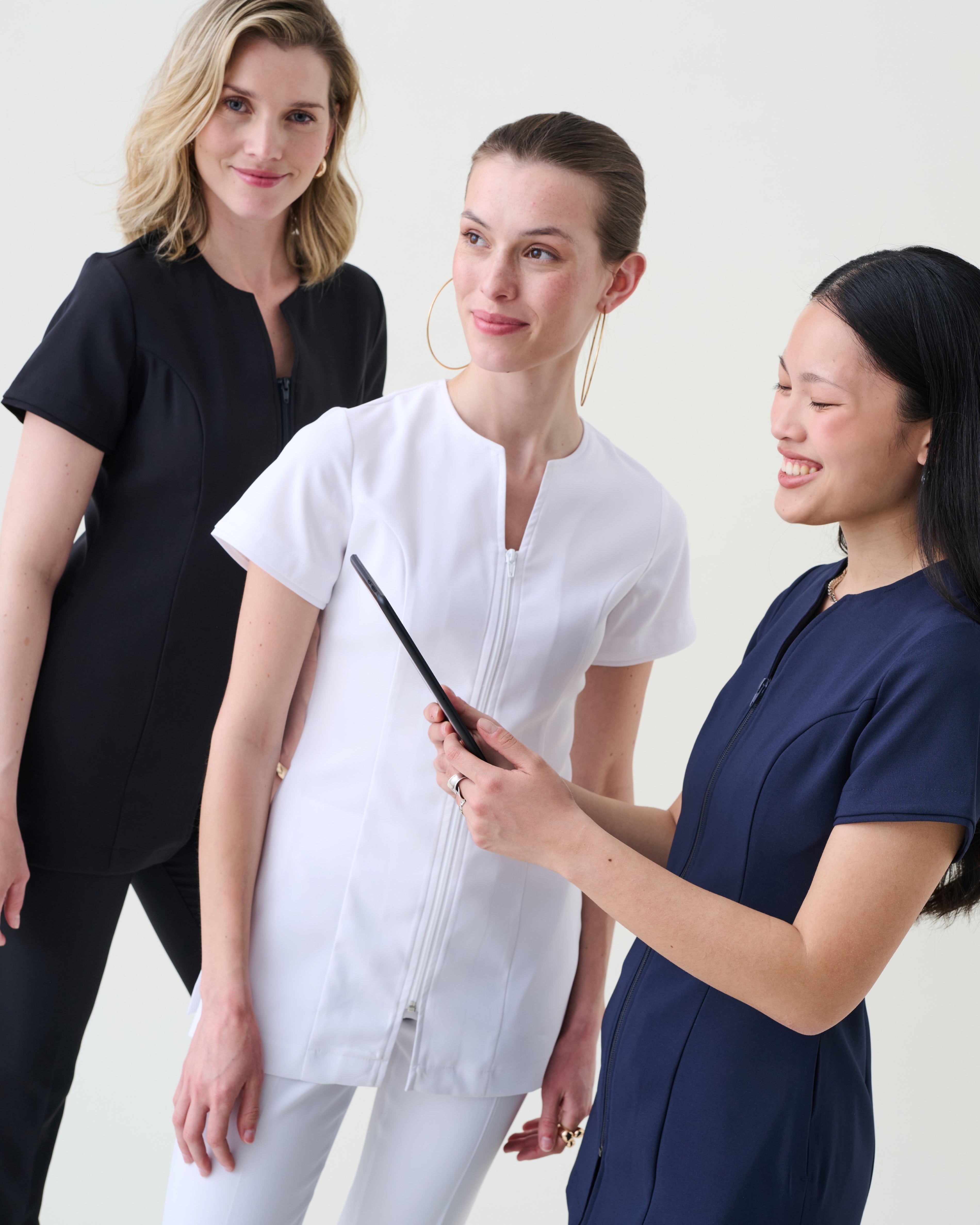 Three women wearing different colored pharmacy scrubs against a white background.