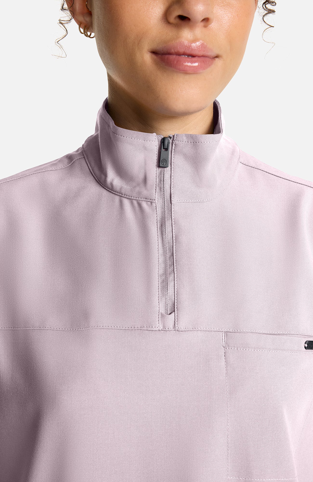 Close-up of a model wearing a light pink quarter-zip pullover with a stand-up collar and a chest pocket, set against a plain light gray background.