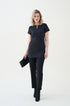 A woman standing against a white background wearing a beauty and hotel black tunic with front pockets and matching black pants.