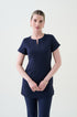 A pharmacist standing against a white background wearing a navy tunic with front pockets and navy pants.