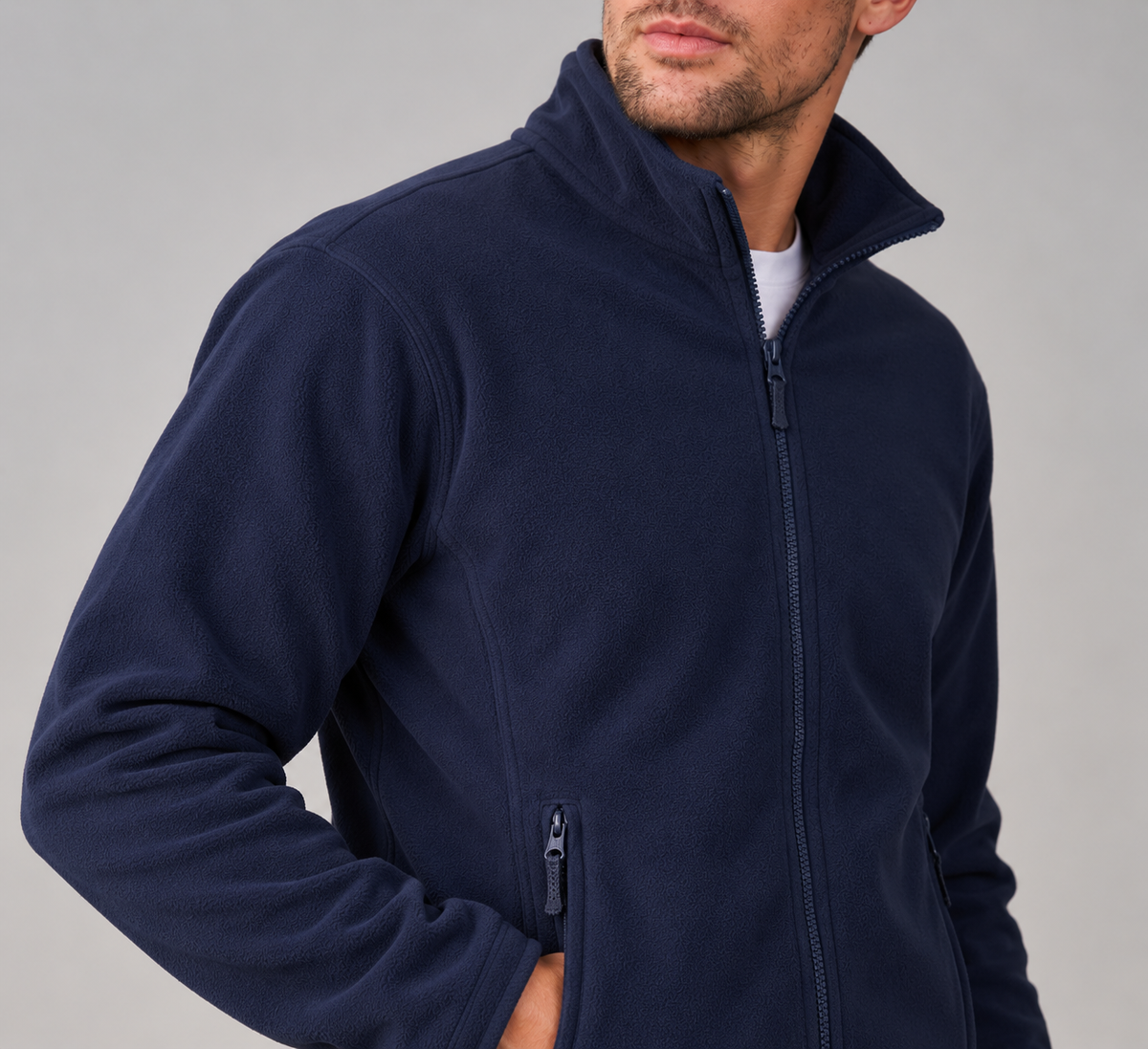 A man wearing a navy blue fleece zip-up jacket, shown from the chin down against a plain light gray studio background.